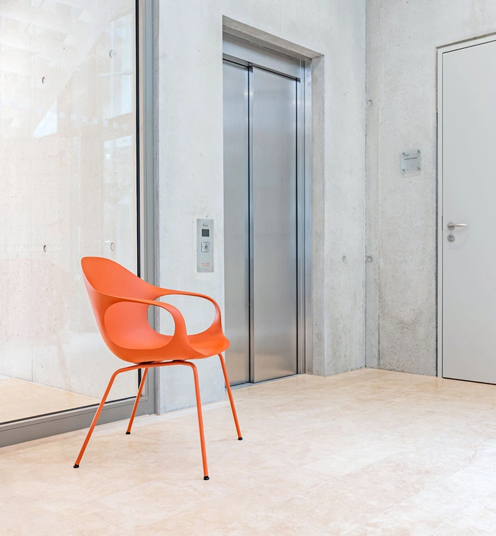 Moderner Aufzug neben orangefarbenem Designerstuhl in heller Lobby